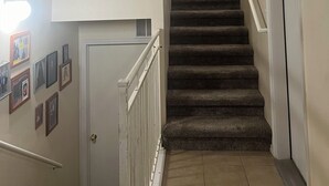 Un escalier muni d’une rampe, avec des marches recouvertes de moquette et une porte en bas.