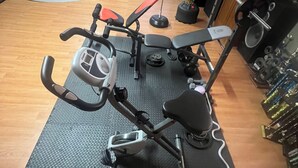 Une salle de sport à domicile équipée d’un vélo elliptique, d’un banc de développé couché et d’un support à squats.