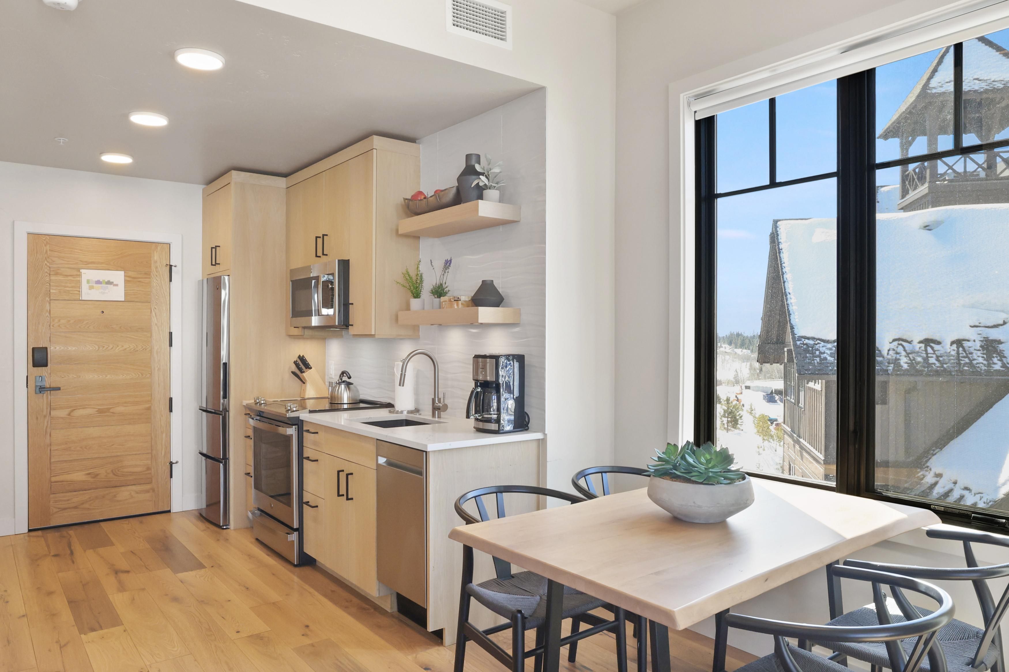 A modern kitchen with wooden cabinets, stainless steel appliances, and a large window offering a view of a snowy landscape.