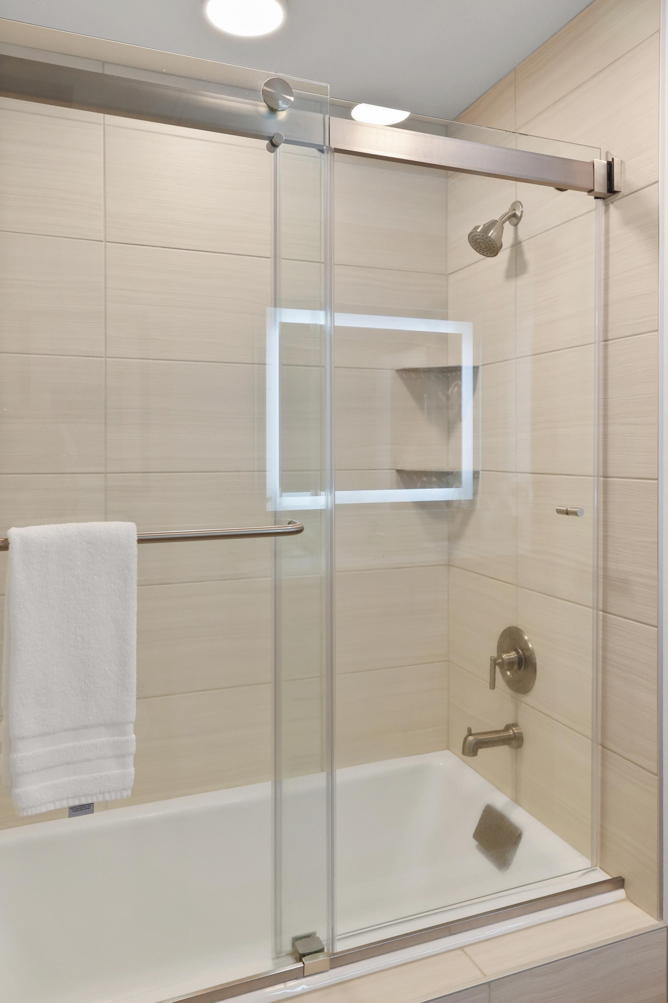 A modern shower enclosure with a glass door, a white towel hanging on a towel bar, and a visible showerhead.