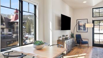 Una sala moderna con un amplio ventanal, un televisor de pantalla plana montado en la pared, una mesa de comedor con sillas y un sillón azul.