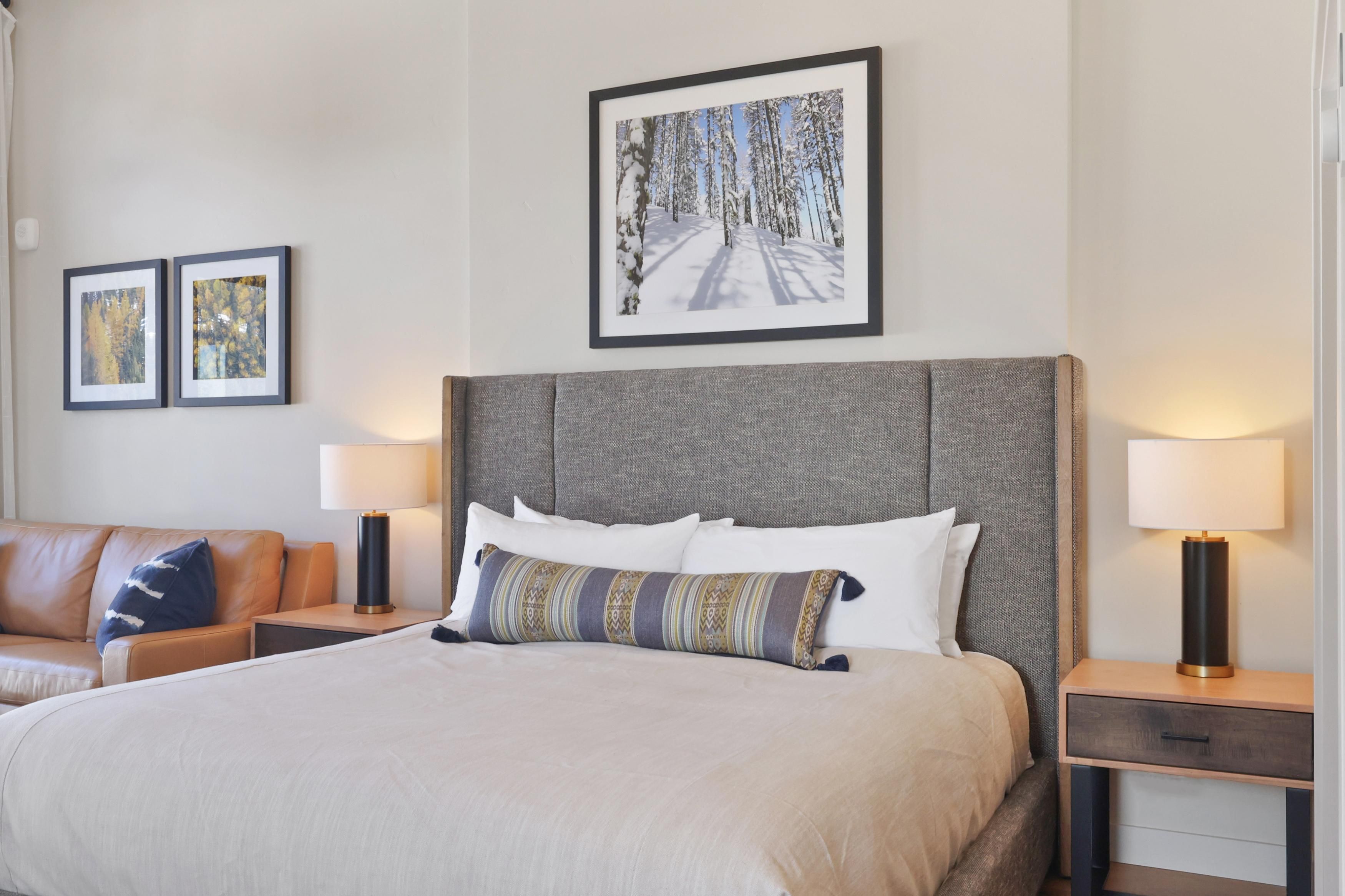 Een hotelkamer met een groot bed, twee nachtkastjes, een slaapbank en twee ingelijste foto's aan de muur.
