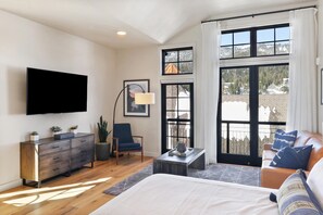 Une chambre moderne avec un lit, une télévision, un fauteuil et une vue sur un paysage enneigé, visible à travers de grandes fenêtres.