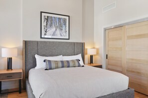 Een hotelkamer met een groot bed, twee bedlampen, een lijst aan de muur en een houten kledingkast.