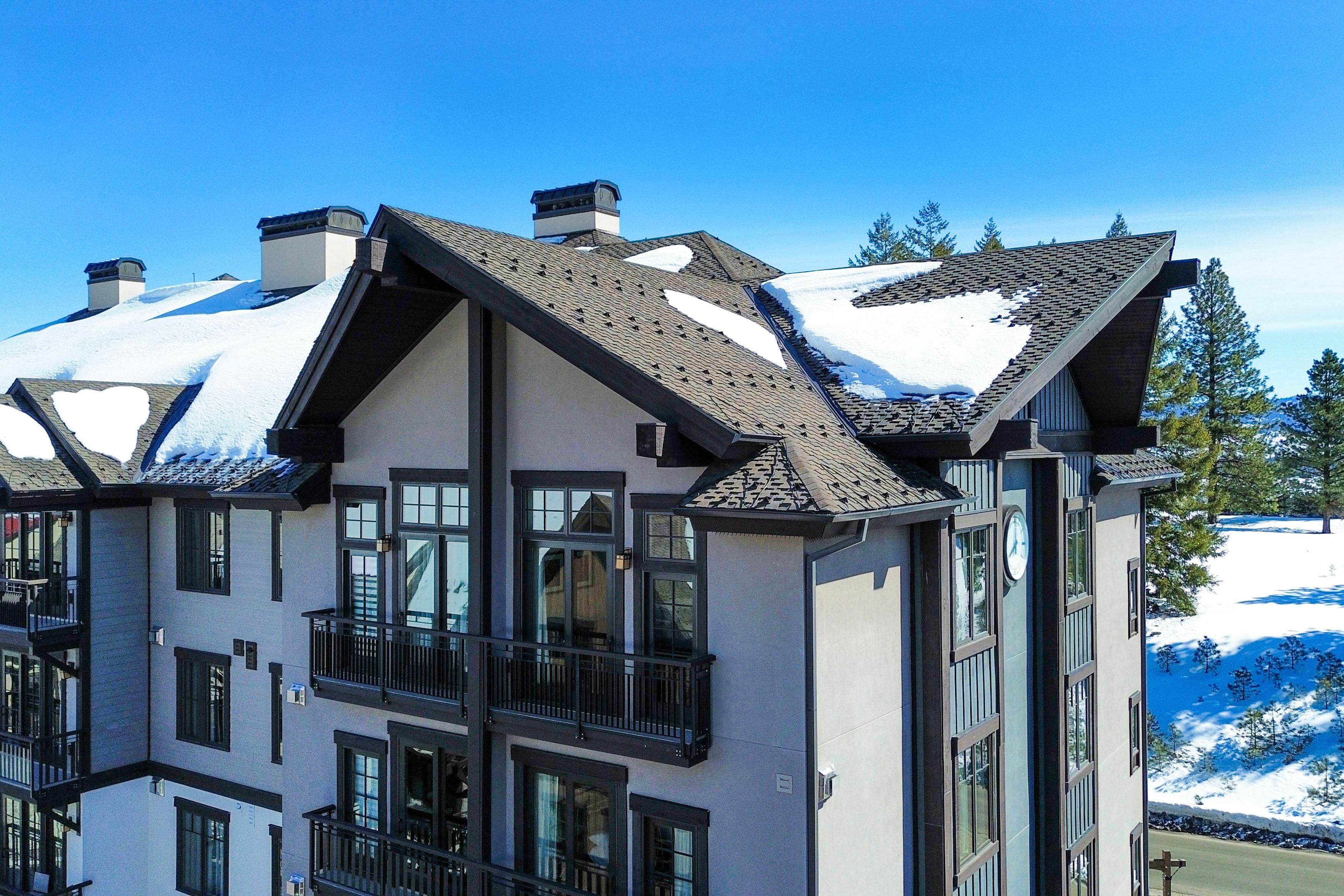 A multi-story building with a snow-covered roof, large windows, and a balcony.