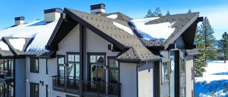 A multi-story building with a snow-covered roof, large windows, and a balcony.