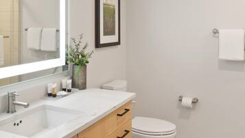 A modern bathroom with a white sink, wooden cabinets, a toilet, and a framed picture on the wall.