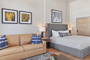A hotel room with a bed, a sofa, two framed pictures on the wall, and a nightstand with a lamp. - Falcon's Nest | Includes Two 1-Day Lift Tickets (Tamarack)