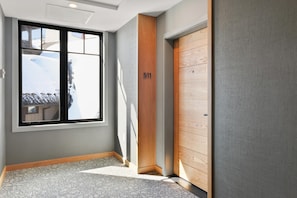 Un pasillo con un ventanal grande, una puerta de madera con un número y una alfombra estampada.