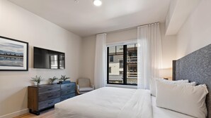 Una habitación de hotel moderna con una cama grande, un tocador, una silla y una ventana con vistas al exterior.