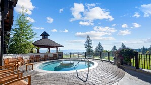 Ein runder Pool im Freien mit einer Whirlwanne, umgeben von Holzstühlen und einem Pavillon.