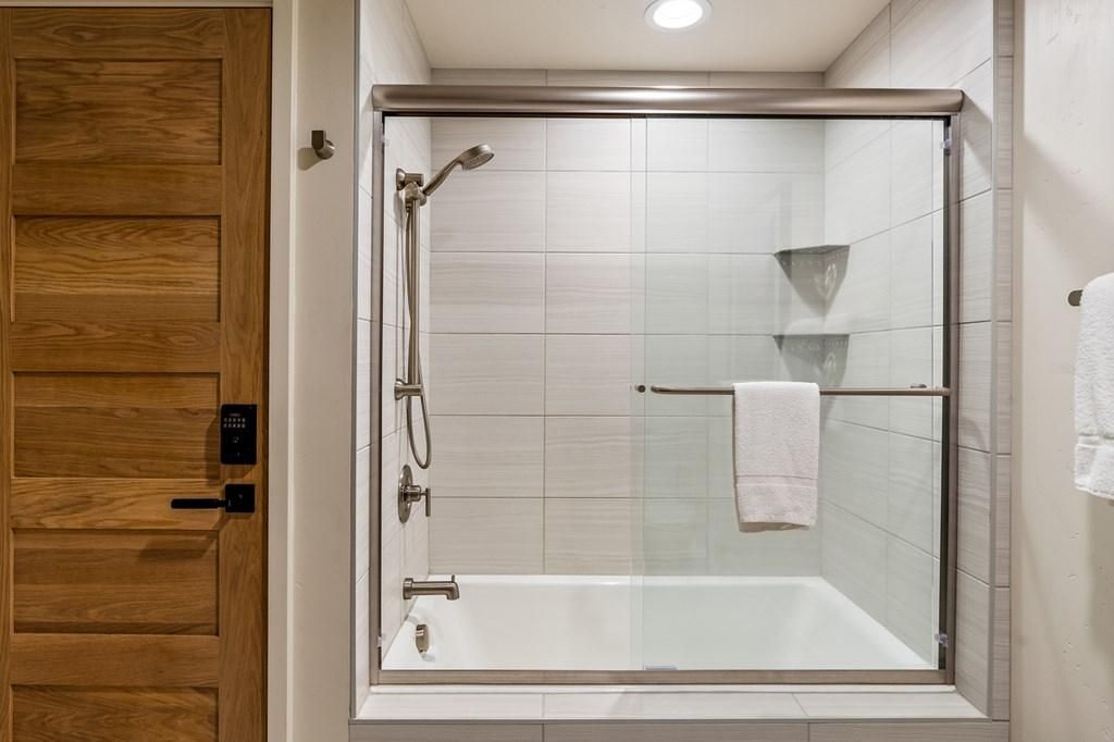 Un baño moderno con ducha de vidrio, puerta de madera y una toalla blanca colgada en un perchero.