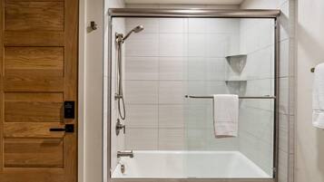 Un baño moderno con ducha de vidrio, puerta de madera y una toalla blanca colgada en un perchero.