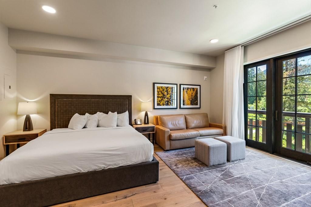 A modern bedroom with a large bed, a leather sofa, and a view through a glass door.