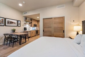 A compact hotel room with a bed, a dining area with a table and chairs, a kitchenette, and a wardrobe. - Makin Memories | Includes Two 1-Day Lift Tickets (Tamarack)