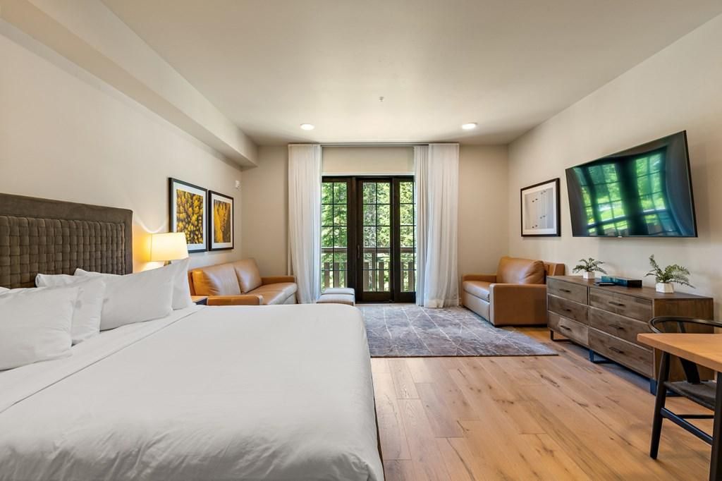 A hotel room with a large bed, a sofa, a desk, and a TV mounted on the wall.