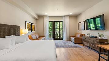 A hotel room with a large bed, a sofa, a desk, and a TV mounted on the wall.