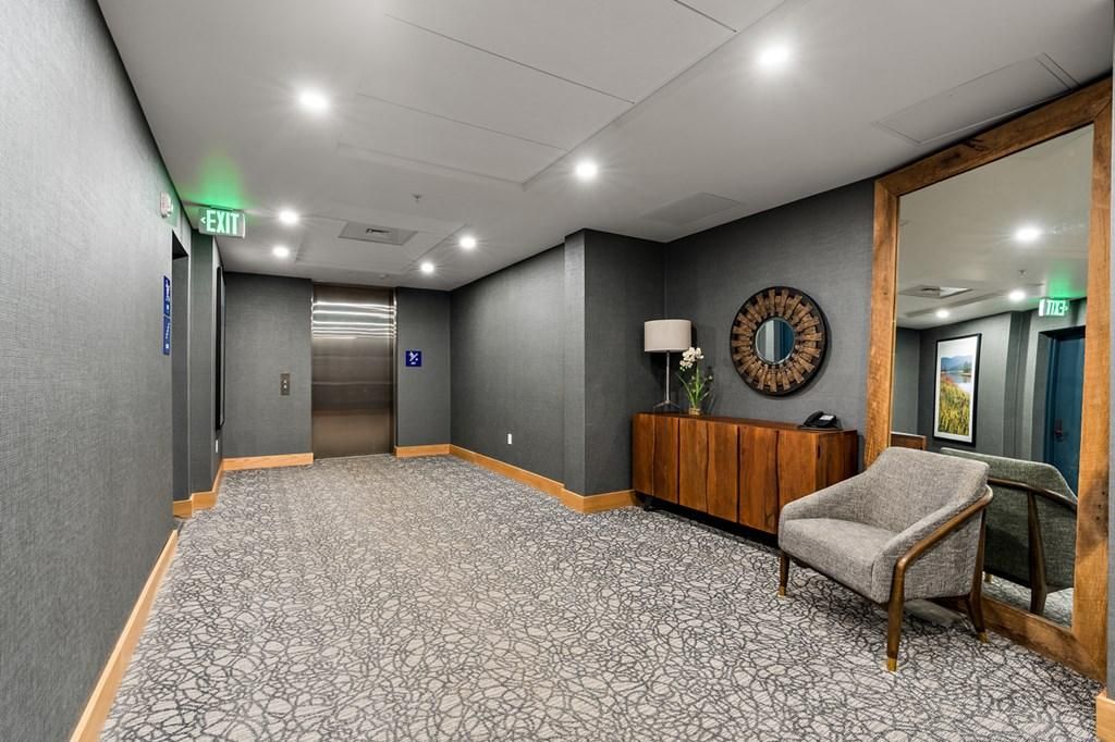 A hotel lobby with a patterned carpet, a wooden cabinet with a mirror, a sofa, and an elevator.