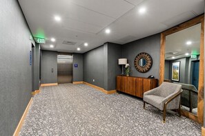 Un hall d’hôtel avec un tapis à motifs, un meuble en bois doté d’un miroir, un canapé et un ascenseur.