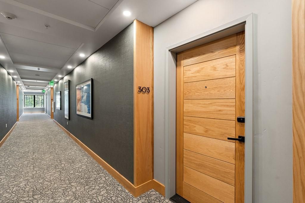 A hallway with a wooden door labeled '303', a patterned carpet, and framed pictures on the wall.