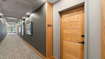 A hallway with a wooden door labeled '303', a patterned carpet, and framed pictures on the wall.
