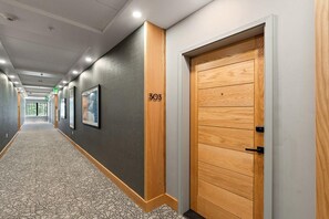 Un couloir avec une porte en bois portant le numéro « 303 », une moquette à motifs et des tableaux encadrés accrochés au mur.