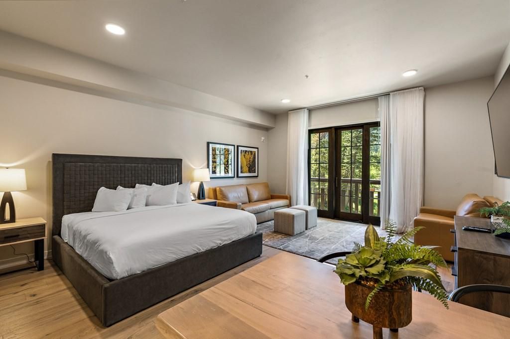 A modern hotel room with a large bed, a sofa, a desk, and a view of greenery through the window.