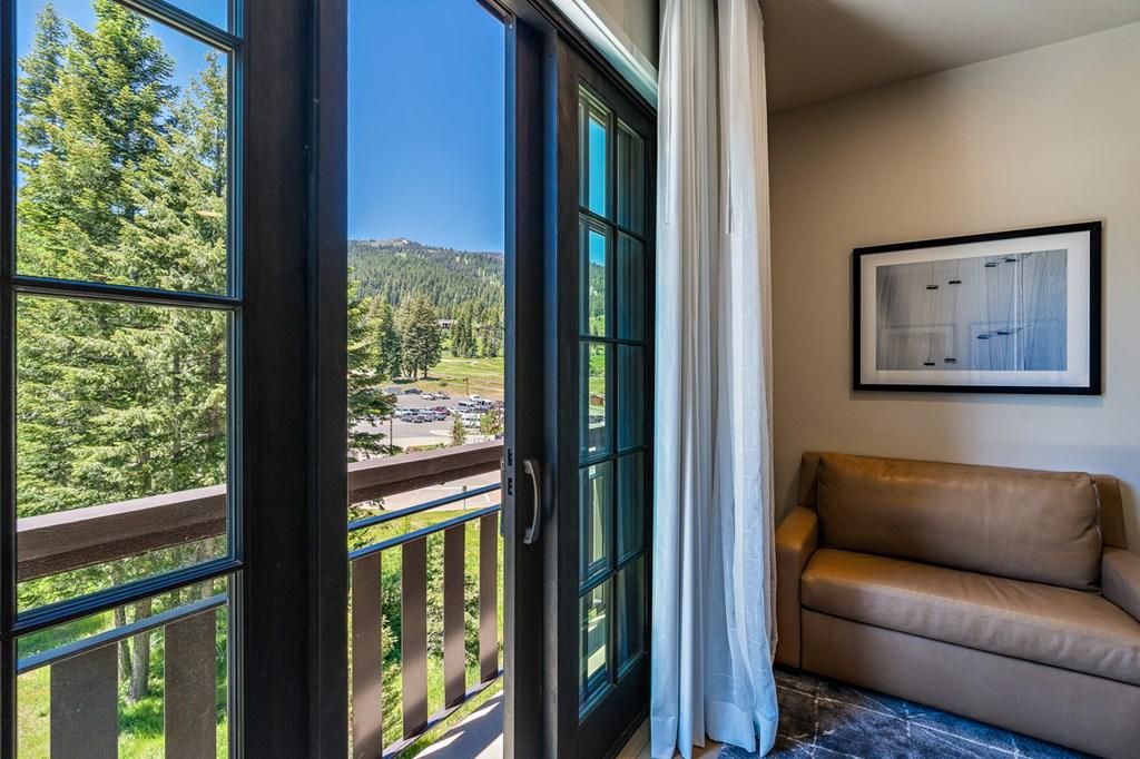 A room with a view of a forest and a road, a beige sofa, and a framed picture on the wall.