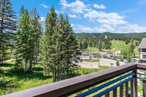 A view from a balcony overlooking a parking lot, a building, and a forested area.