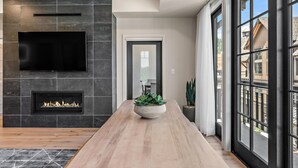 A modern living room with a fireplace, a flat-screen TV, and a large window. - Sassafras Suite | Includes Two 1-Day Lift Tickets (Tamarack)