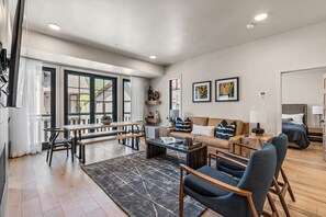 Un salon spacieux doté d’une grande fenêtre, d’un canapé, d’une table basse et d’un coin repas avec un banc.