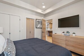 Une chambre moderne avec un grand lit, une commode en bois, un téléviseur à écran plat et un coin bureau agrémenté de plantes.