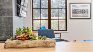 Une pièce avec une grande fenêtre, une chaise bleue, une table ornée d’une plante décorative et un tableau encadré accroché au mur.