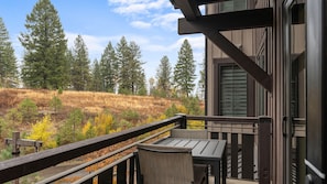 A balcony with a table and chairs, overlooking a forested hillside with autumn foliage. - Mountain Condo | Includes Two 1-Day Lift Tickets (Tamarack)