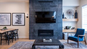 Una sala de estar moderna con chimenea, televisor de pantalla plana y comedor con mesa y sillas de madera.