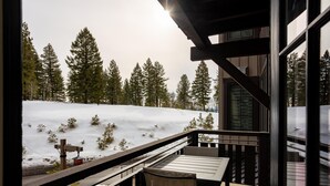 Una terraza de madera con una mesa y sillas que da a un paisaje nevado con árboles.