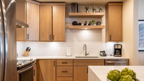 Una cocina moderna con armarios de madera, un refrigerador de acero inoxidable, horno empotrado, un lavamanos y una cafetera.
