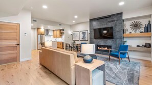 A modern living room with a fireplace, a TV mounted on the wall, and a dining area with wooden furniture. - Mountain Condo | Includes Two 1-Day Lift Tickets (Tamarack)
