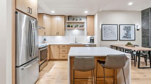 Eine moderne Küche mit einem Edelstahlkühlschrank, Holzschränken, einer Marmorarbeitsplatte und einem Essbereich mit Tisch und Stühlen.