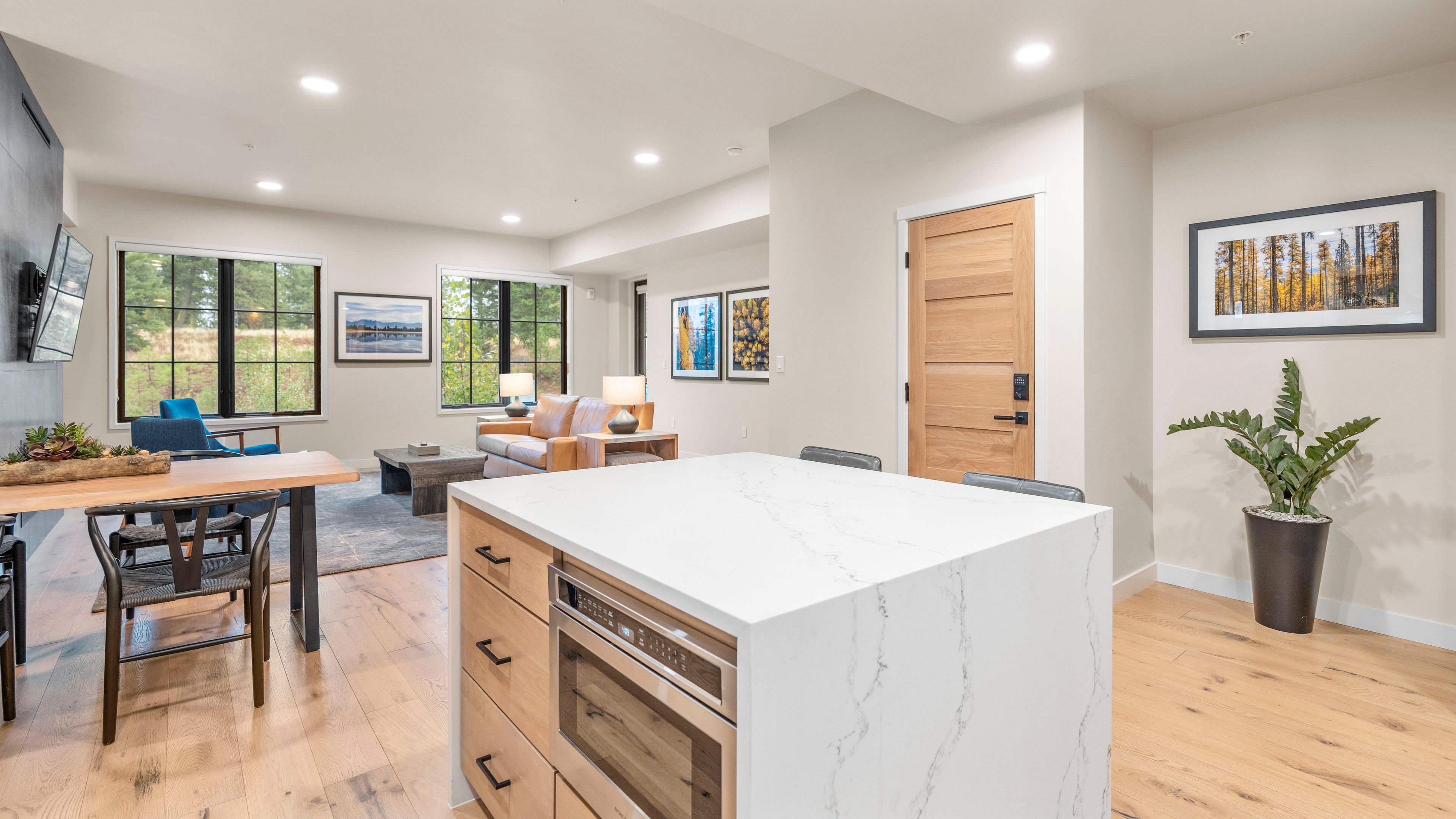 A modern kitchen with a marble island, wooden cabinets, and a dining area with a blue chair.