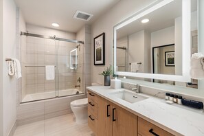 A modern bathroom with a glass-enclosed shower, a bathtub, a toilet, and a large mirror.