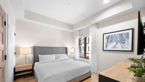 Un dormitorio moderno con una cama grande, mesitas de noche, un escritorio y una ventana con cortinas.