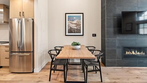 Une cuisine moderne avec un réfrigérateur en acier inoxydable, une table à manger en bois avec des chaises, une cheminée et un tableau encadré au mur.