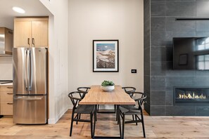 Una cocina moderna con un refrigerador de acero inoxidable, una mesa de comedor de madera con sillas, una chimenea y un cuadro en la pared.