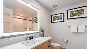 Une salle de bain moderne avec un grand miroir, un lavabo blanc, des meubles en bois et deux tableaux encadrés accrochés au mur.