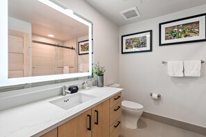 Un baño moderno con un espejo grande, un lavamanos blanco, armarios de madera y dos cuadros en la pared.