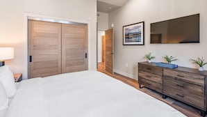 Une chambre à coucher avec un grand lit, une commode, un miroir et une porte donnant sur une autre pièce.