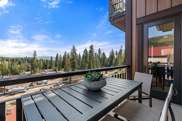 A balcony with a potted plant, a table, and chairs.