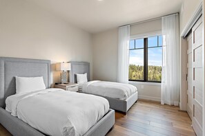 A bedroom with two beds, a nightstand with a lamp, and a window with a view of trees.