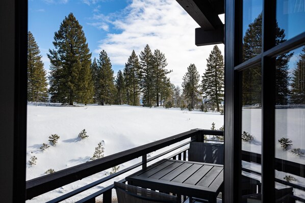 A wooden deck with a view of a snowy landscape and tall evergreen trees. - Post Road Condo | Includes Two 1-Day Lift Tickets (Tamarack)